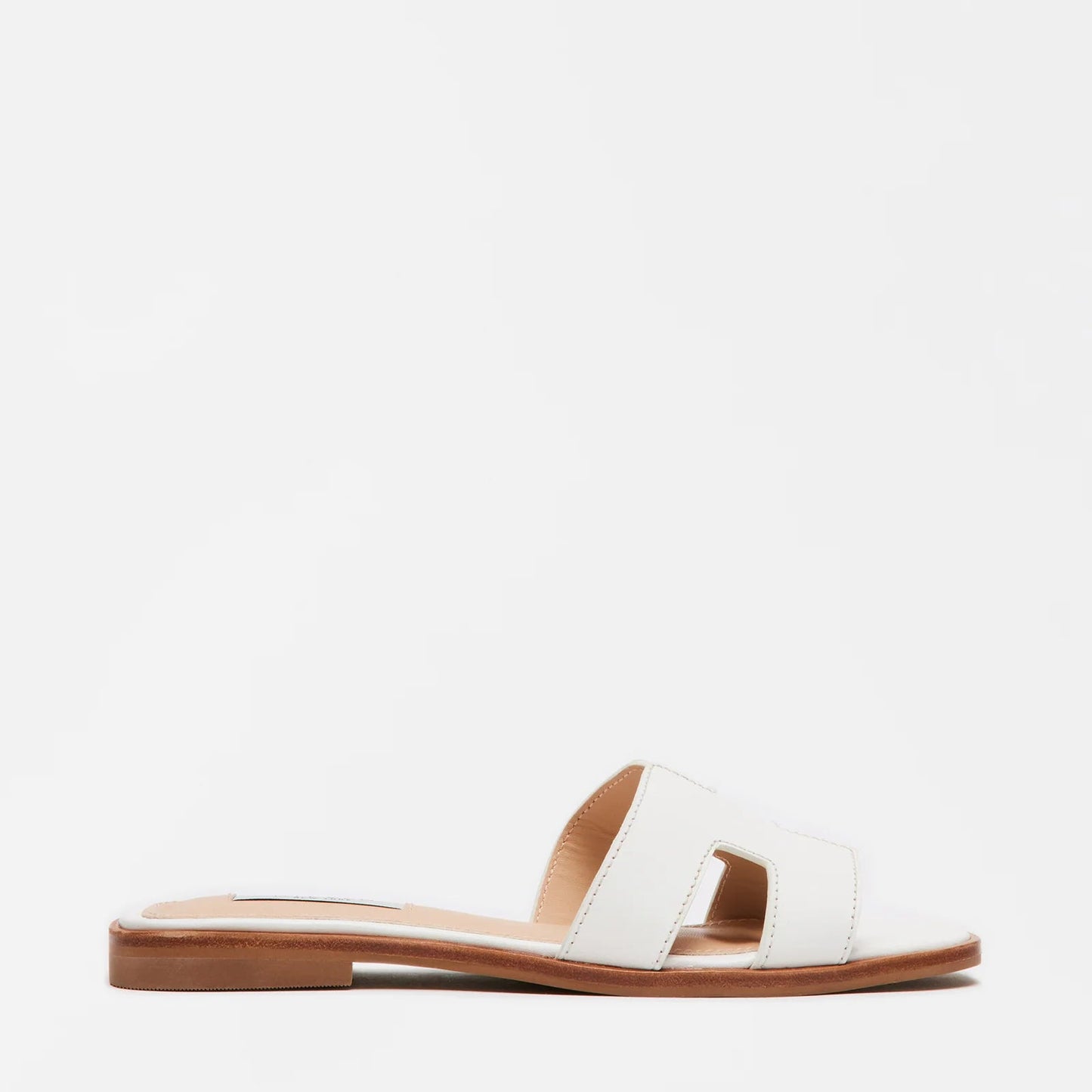 A white flat sandal with geometric cutouts on the strap and a tan sole.