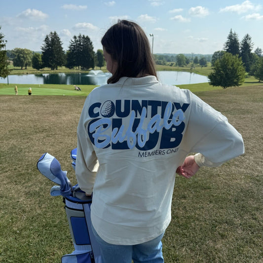 Person on a golf course wearing a 'County Club' shirt with a golf bag in front